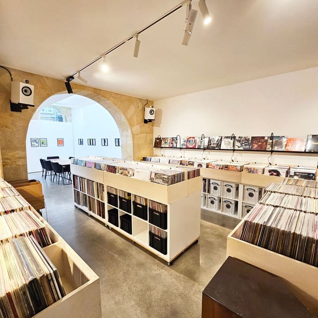 L'intérieur d'Éponyme Vinyle : des bacs de disques en bois clair sous des arches de pierre, des pochettes exposées au mur et un coin d'écoute au fond.