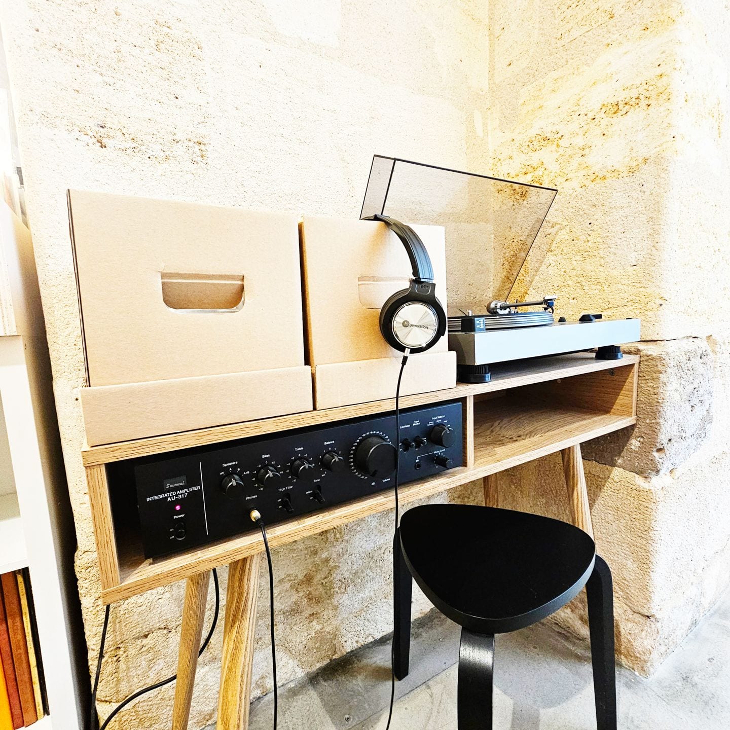 Un point d'écoute dans la boutique : platine, amplificateur et casque posés sur un meuble en bois, contre un mur de pierre