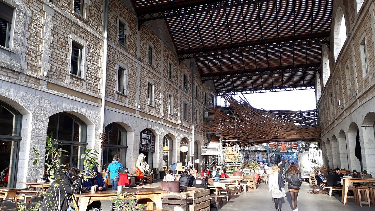 Sous la grande halle de Darwin, à Bordeaux, des visiteurs attablés devant des façades de pierre et une structure de bois.