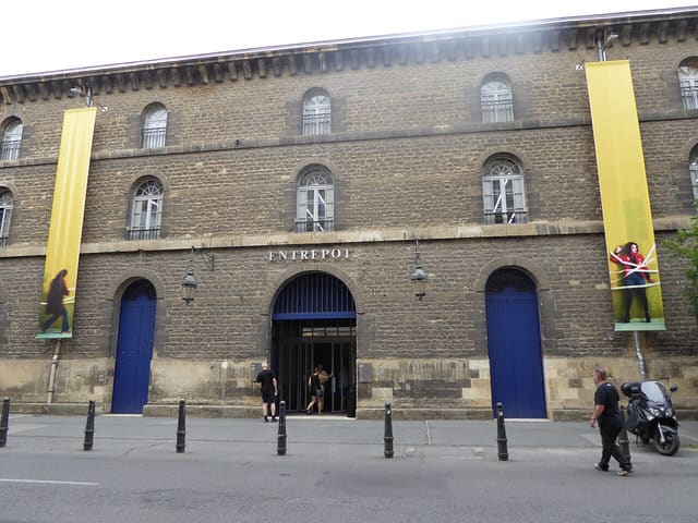 Façade en pierre de l'Entrepôt, bâtiment du Capc à Bordeaux, avec ses deux bannières jaunes et ses portes bleues.