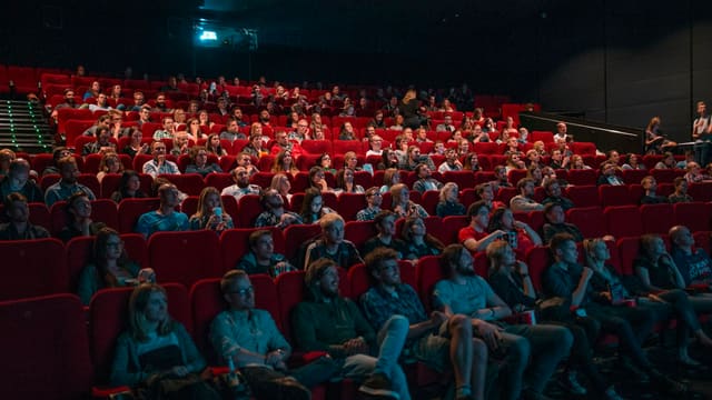 Une salle de cinéma comble, fauteuils rouges, spectateurs tournés vers l'écran